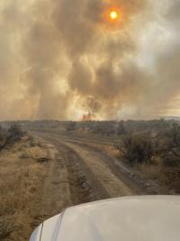 Fire and smoke with blazing sun and dirt trail in foreground.