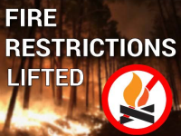 A wooded area with flames burning among the trees. Bold text across the image reads “Fire Restrictions Lifted.” In the bottom right corner, a graphic shows a red circle with a slash over a flame icon.