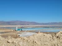 Towers and other mining related structures are alongside manmade ponds with mountains in the background.
