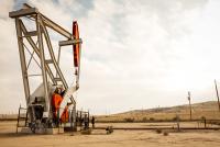 A white and red pump jack rises over dried grass hills.