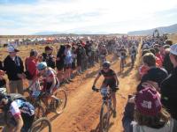 A crowd cheers on several bike racers on a dirt trail.