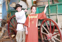two children in old fashioned garb standing next to display of a covered wagon