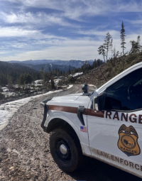 A photo of the front of a law enforcement vehicle on a dirt road with a scenic landscape in the background