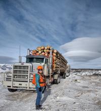 Woman forester stands next to logging truck on BLM lands.