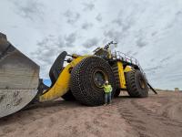 Person in a white hard hat and neon yellow safety vest pointing towards a rocky cliff face at a mining or excavation site.