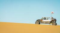 An off road vehicle ascends a gradual dune.