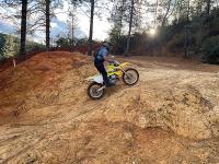 A dirt bike rides up a brown hill in the forest.