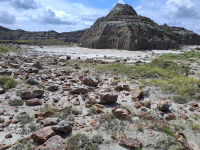 Rock-strewn desert landscape with a large, rounded rocky hill under a partly cloudy sky.