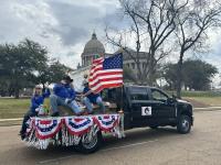 A group of people sit on a truck bed decorated with an American flag and bunting. 