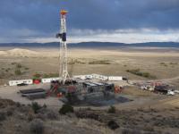 An oil and gas drill rig and pad are seen on an open plain with dark clouds overhead