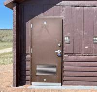 Campground vault toilet with bullet holes.