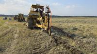 Three tractors using specialty plows bury power and fiber optic cable lines across a prairie landscape.