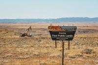 A BLM sign for the Vernal Field Office with an oil derrick in the background.