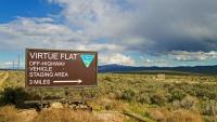 Sign reading “Virtue Flat Off‑Highway Vehicle Staging Area, 3 miles” stands in a sagebrush landscape with distant mountains under a partly cloudy sky.