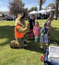 Seymour the Antelope kneels to greet children during Kemmerer Outdoor Discovery Day at Triangle Park with blue skies and green grass