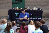 Ranger sits on the ground presenting a skull to young children.