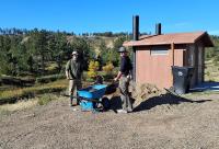 Two volunteers load a wheelbarrow from a pile of gravel