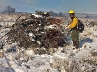 A firefighter starts a prescribed burn in a pile of wood in an area covered in snow. Photo by George Jolicoeur, BLM.