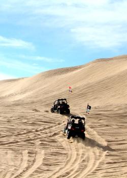 Two OHVs climb a dune.