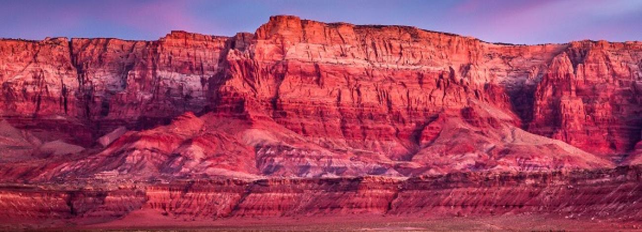 Clouds are pink and blue above red-orange cliffs.