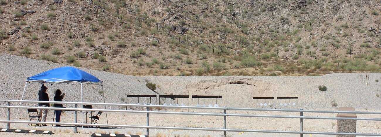 two people shoot at an outdoor shooting range with hanging targets