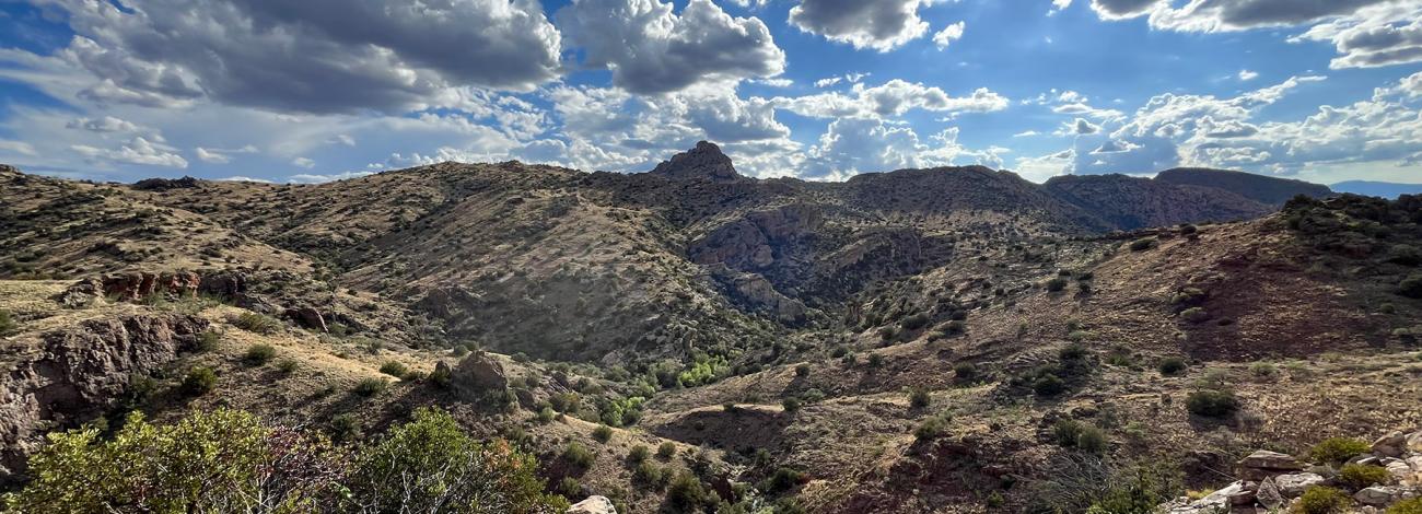 Sunlit rocky landscape with scattered shrubs under a partly cloudy blue sky.
