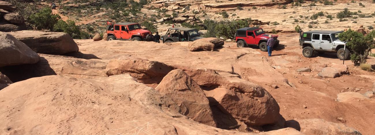 Jeeps travel a desert landscape, over sandstone domes