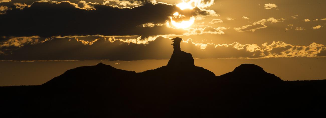 Geological formation sticks up above horizon with yellow sunset behind