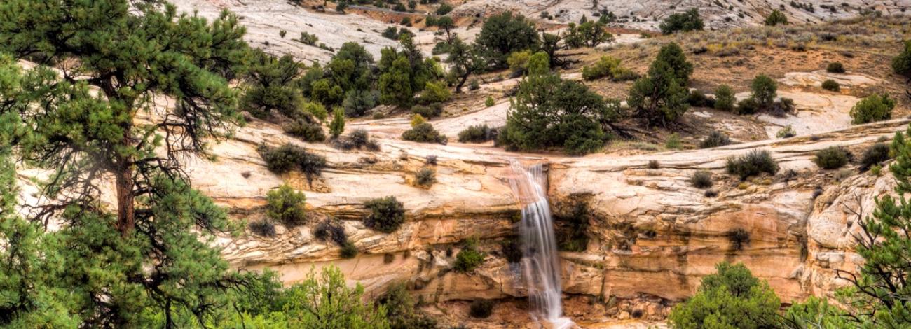 waterfall coming off rocky cliff with slickrock in background