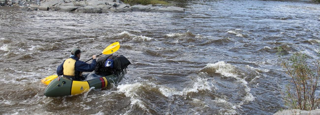 A person kayaking along the Birch Creek Wild and Scenic River in Alaska with trees and rocks lining the bank in the background. Photo by BLM.