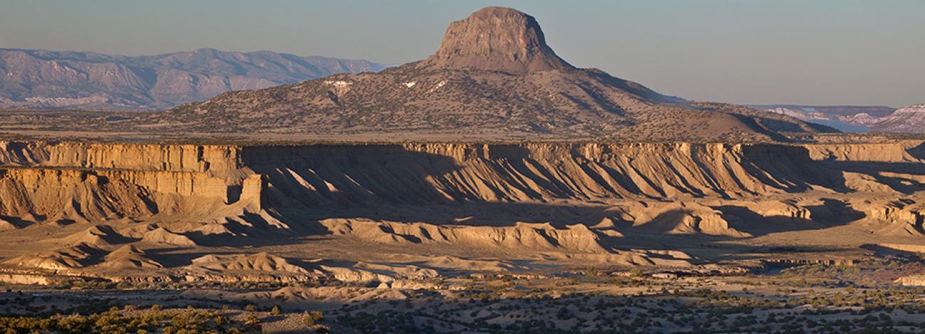The volcanic plug of Cabezon Peak with long shadows on the cliffs in the foreground.