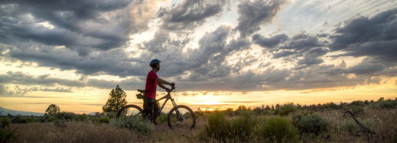 Biker on trail looking out at sunset.