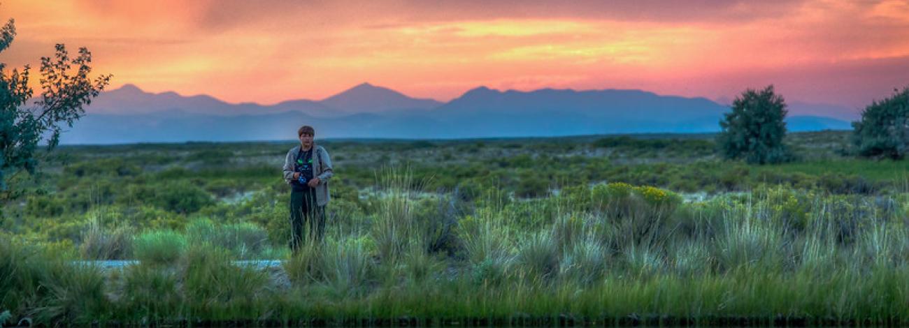 sunset over mountains in background with person fishing in foreground