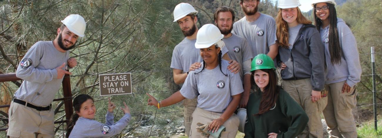 Group of AmeriCorps wearing hard hats and posing for group photo during trail work.