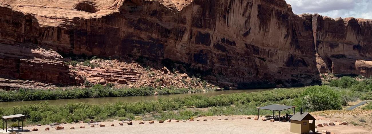 Broad view of Colorado River Day Use Area with red rock cliffs and shade structure.