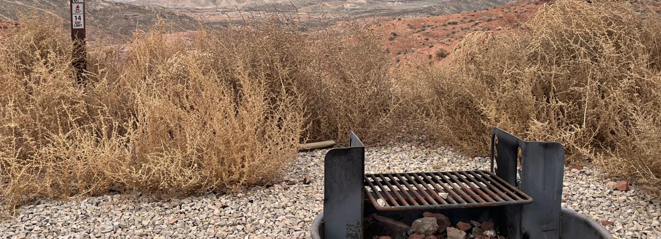 Graveled campsite against a backdrop of rolling red dirt hills and the Pine Valley Mountains. 
