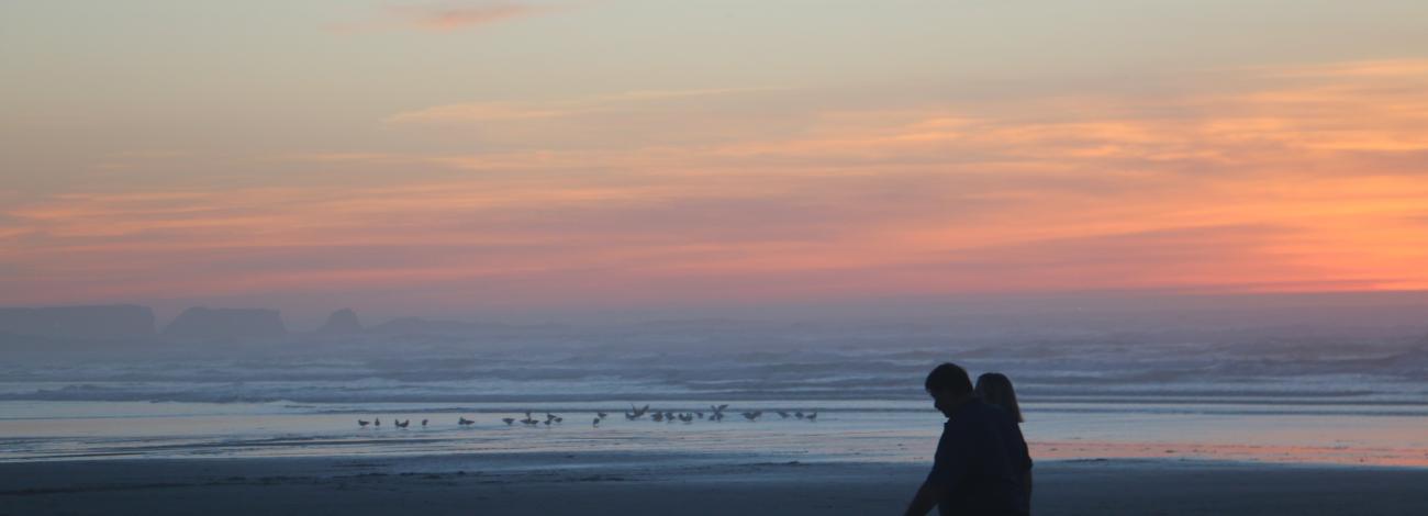 Two people walk across Bastendorff Beach at sunset.