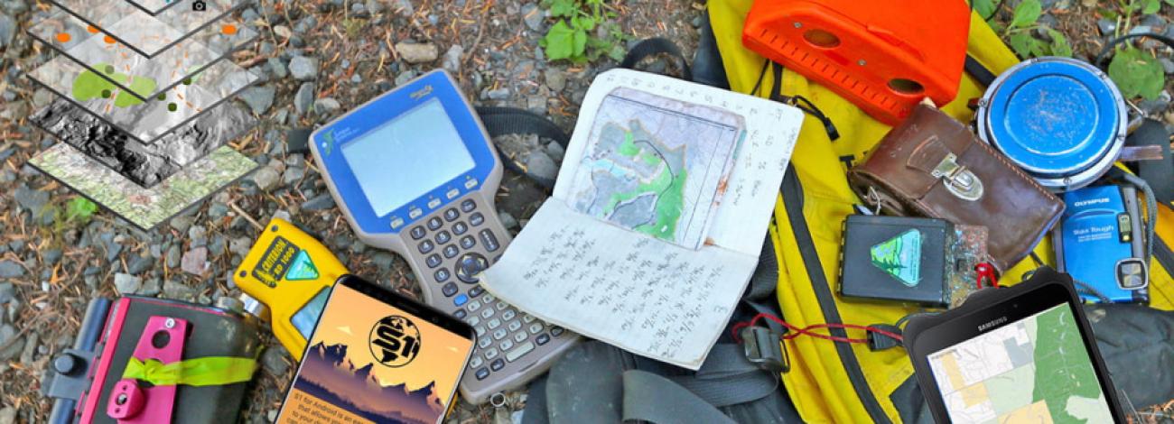 A selection of gear used for field data collection laying on the ground, including paper and electronics