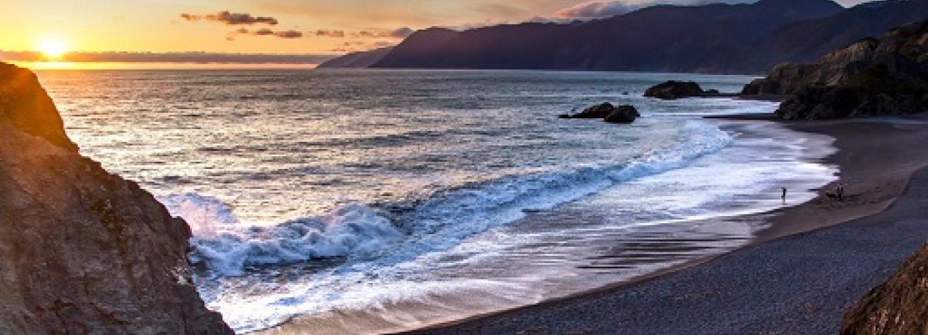 A couple and their dog enjoy the beach as the sun sets over the Pacific Ocean at Black Sands Beach, California, photo by Bob Wick, BLM