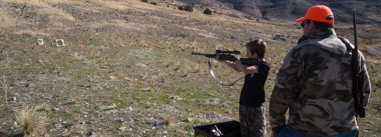 Boy shooting at a target with man watching