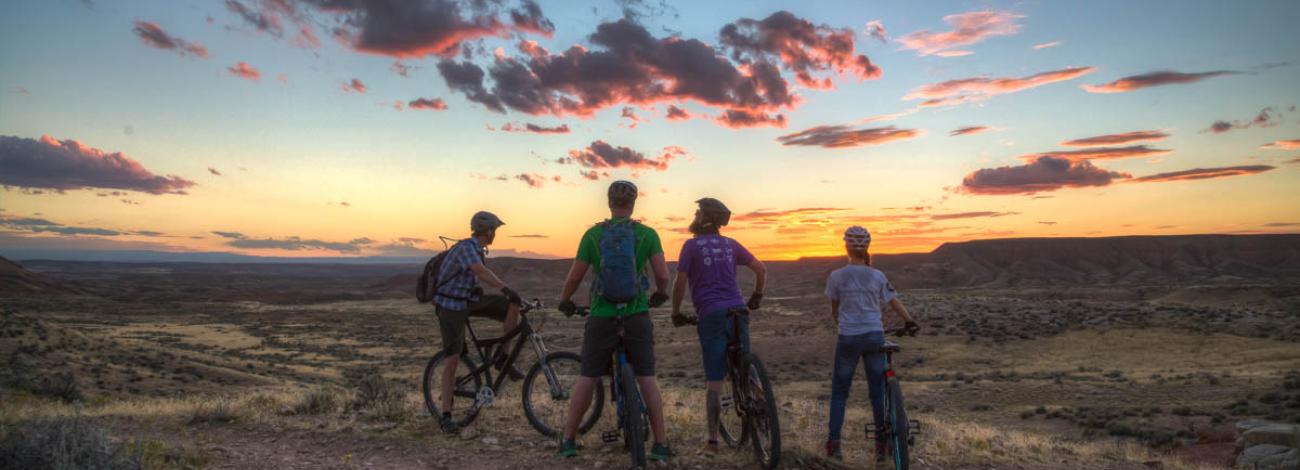 Four bike riders in the Utah desert facing a sunset