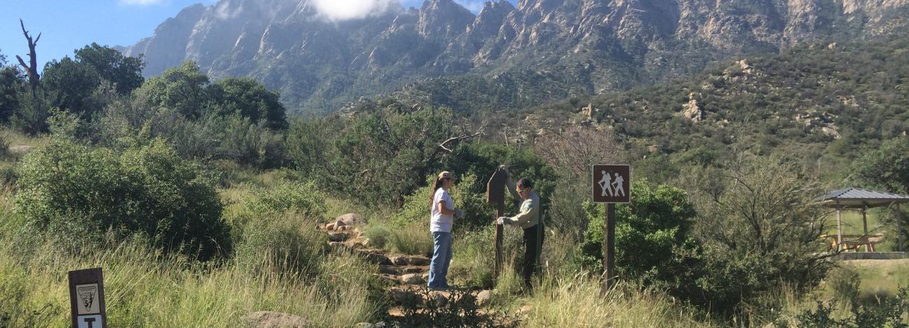 mountains in background on bluebird skys day. Two Volunteers work on Trail