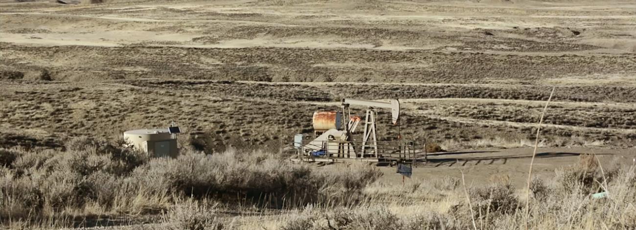 rolling Wyoming sagebrush landscape in shades of tan with a oil pump jack and tanks painted to blend.