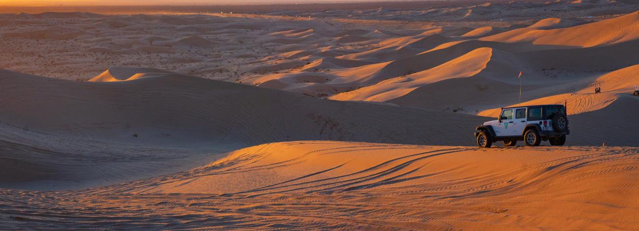 Jeep overlooks sand dunes at sunset