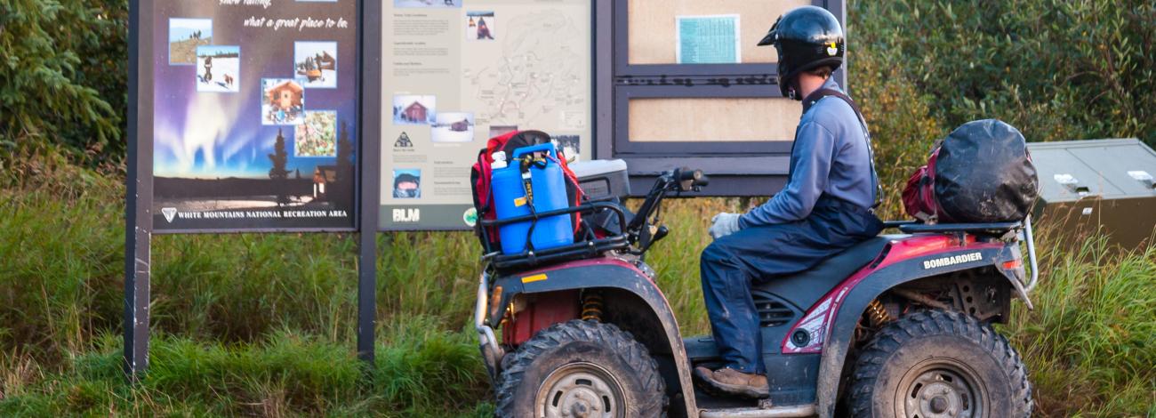 A rider on an ATV looks at the trailhead information kiosk.