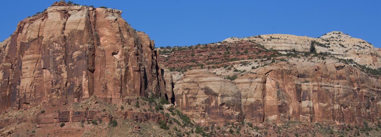 A vehicle drives down a two-track road with red sandstone cliffs looming.