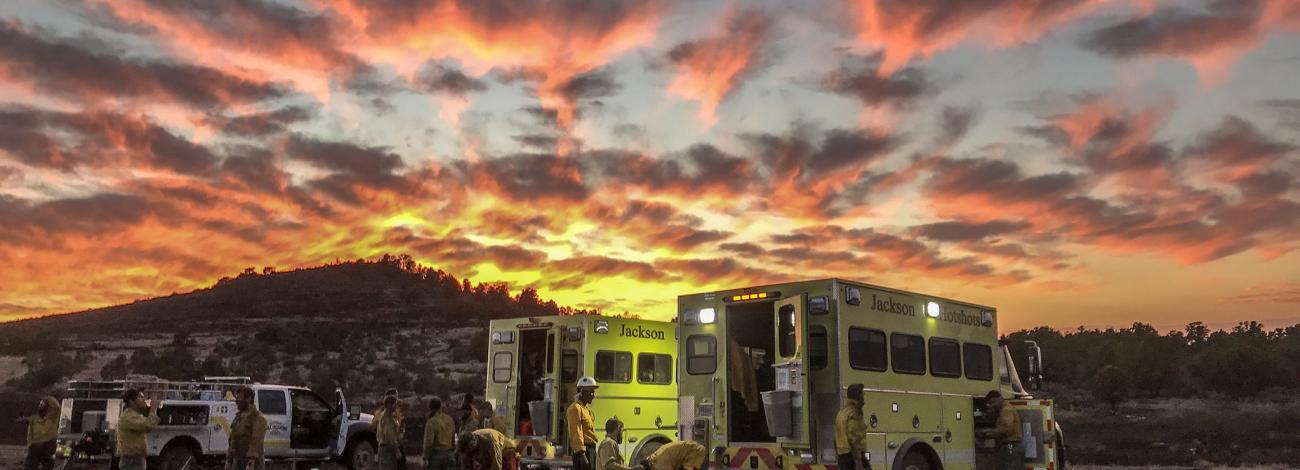 The sun sets behind two Jackson Hotshots trucks and crew.