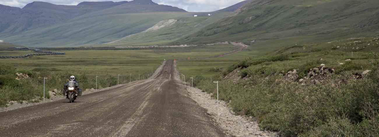 Motorcyclist riding on the Dalton Highway, a strip of gravel road between tundra-carpeted hills. Photo by Bob Wick BLM 2014
