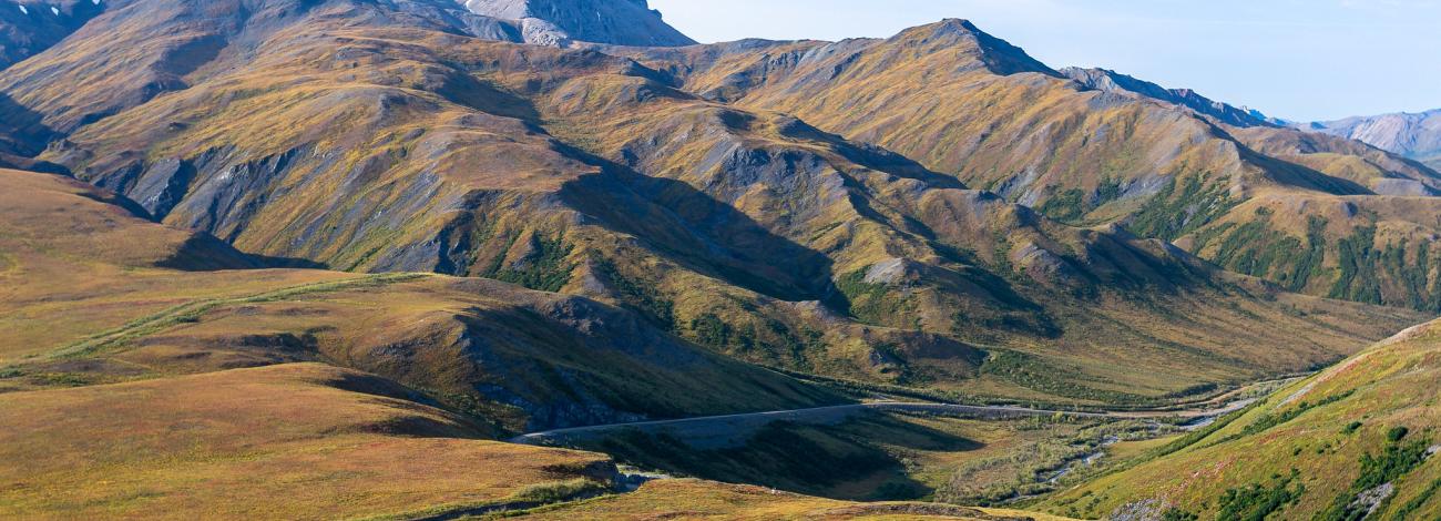 Colorful grassy hills in the foreground with mountains and blue skies.