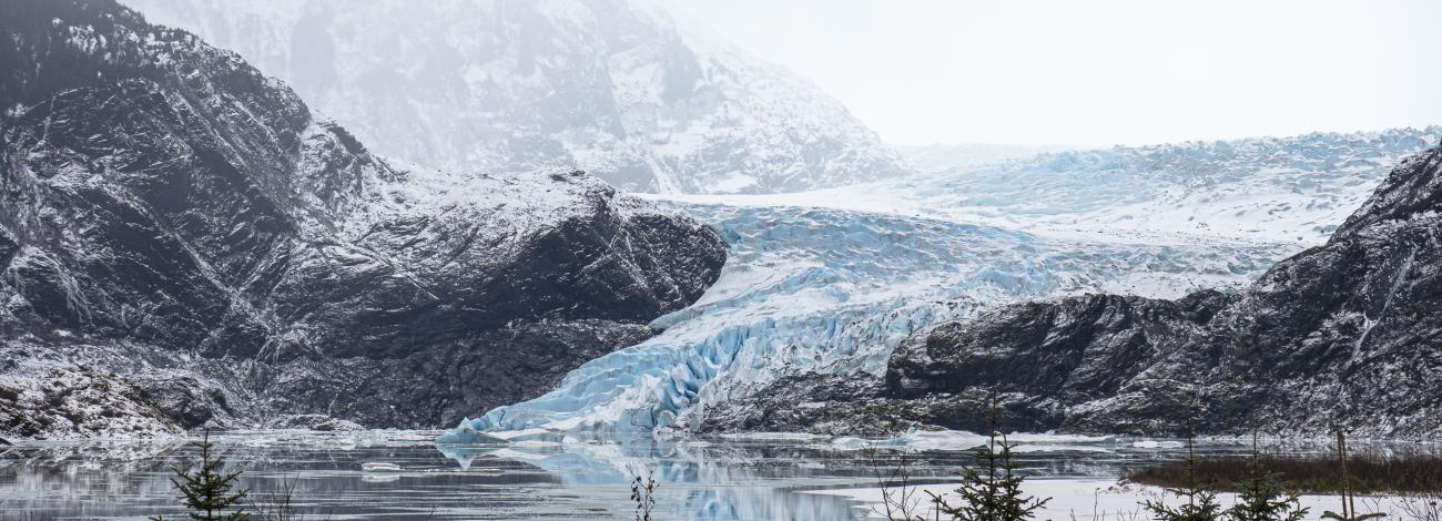 A glacier behind glacial lake between tree-filled mountains